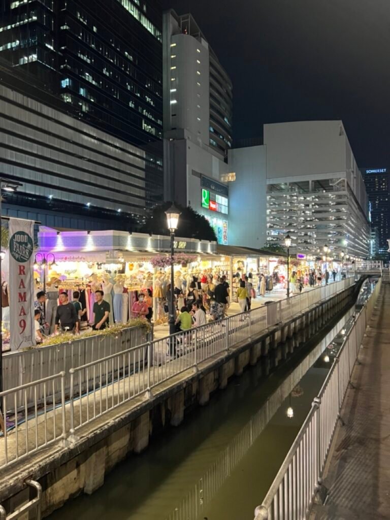 Allée principale du marché Jodd Fairs à Bangkok, située entre des buildings modernes, avec ses stands lumineux.