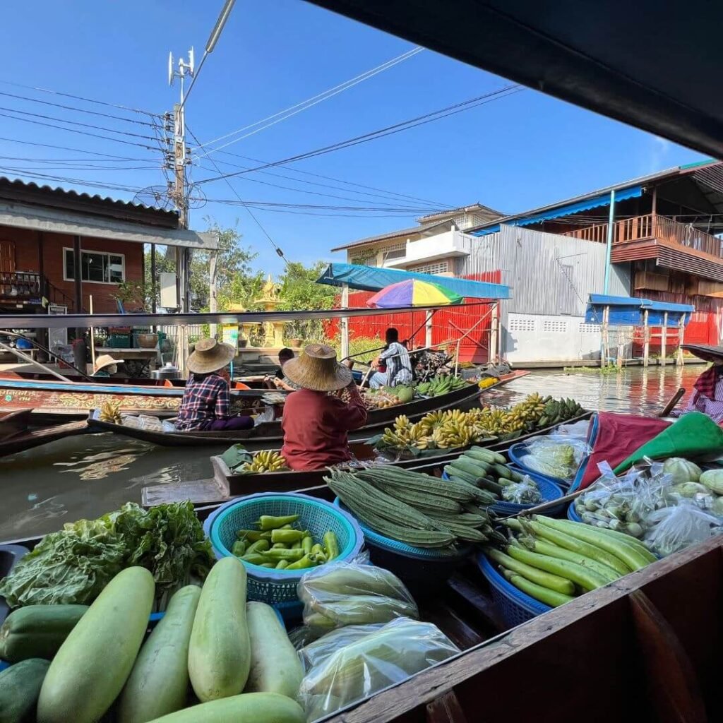 Des vendeurs sur des bateaux remplis de légumes frais au marché flottant, un exemple de l'ambiance animée des marchés en Thaïlande.