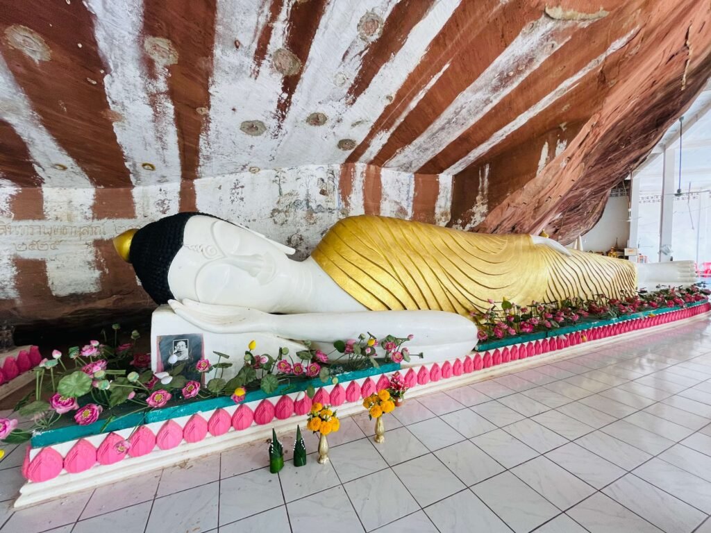 Statue de Bouddha allongé avec une robe dorée dans un temple en Thaïlande, entourée de décorations florales.